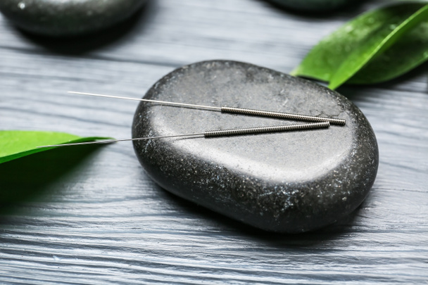 Acupunctuur naalden en spa steen op houten achtergrond - Foto, afbeelding