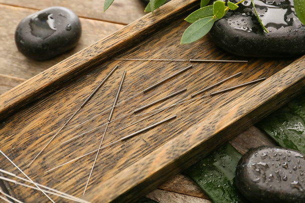 Stand con aghi per agopuntura e pietre termali su sfondo in legno - Foto, immagini