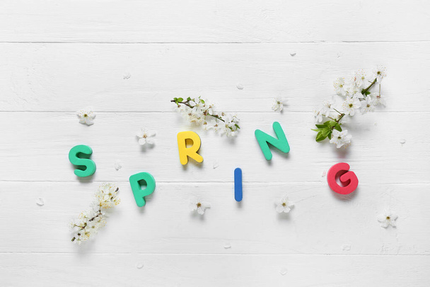 Word SPRING and beautiful blooming branches on light wooden background - Fotografie, Obrázek