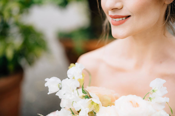 Χαμογελαστή νύφη σε ένα όμορφο φόρεμα με ένα μπουκέτο λουλούδια σε φόντο πράσινου δέντρου σε μπανιέρα - Φωτογραφία, εικόνα