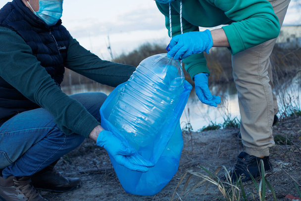 volontari raccolgono bottiglie di plastica in sacchetti, primo piano delle mani, il concetto di ecologia e protezione della terra. - Foto, immagini