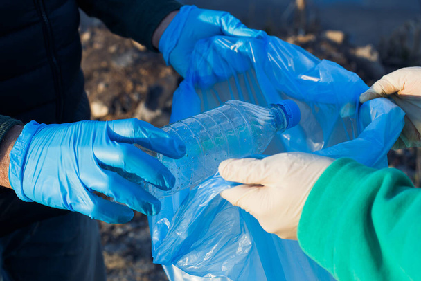 vrijwilligers verzamelen plastic flessen in zakken, close-up van handen, het concept van ecologie en bescherming van de aarde. - Foto, afbeelding