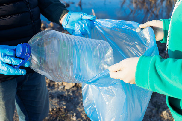 Freiwillige sammeln Plastikflaschen in Tüten, Nahaufnahme der Hände, das Konzept der Ökologie und des Schutzes der Erde. - Foto, Bild