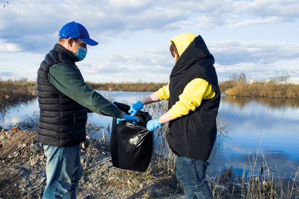 voluntarios recogen botellas de plástico en bolsas en la orilla del río, el concepto de ecología y protección de la tierra. - Foto, imagen
