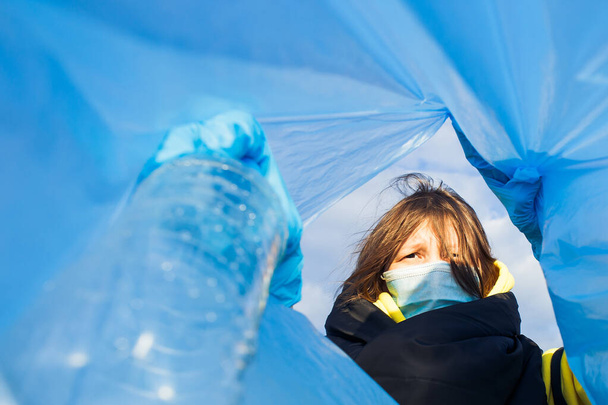 μια γυναίκα πετάει ένα πλαστικό μπουκάλι σε μια τσάντα κάτω από τα σκουπίδια, κοντινό πλάνο, η έννοια της οικολογίας και της προστασίας της γης. - Φωτογραφία, εικόνα
