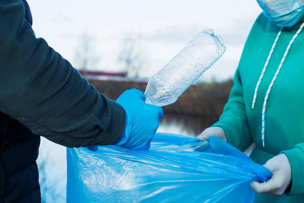 εθελοντές συλλέγουν πλαστικά μπουκάλια σε σακούλες, κοντινό πλάνο των χεριών, η έννοια της οικολογίας και της προστασίας της γης. - Φωτογραφία, εικόνα