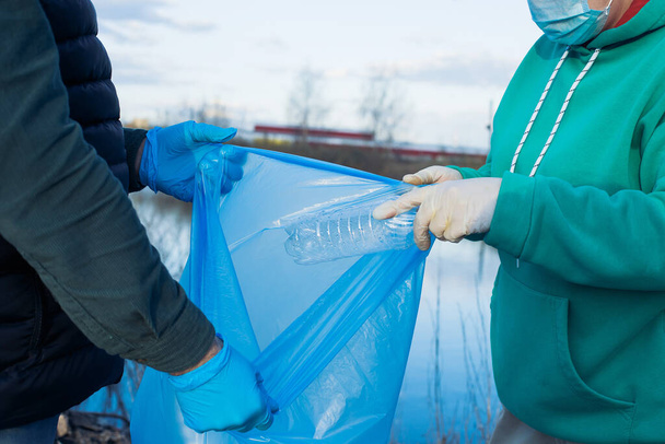 εθελοντές συλλέγουν πλαστικά μπουκάλια σε σακούλες, κοντινό πλάνο των χεριών, η έννοια της οικολογίας και της προστασίας της γης. - Φωτογραφία, εικόνα