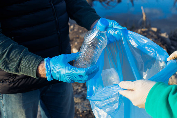 voluntarios recogen botellas de plástico en bolsas, primer plano de las manos, el concepto de ecología y protección de la tierra. - Foto, Imagen