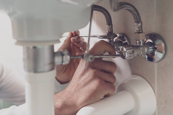 Professional plumber fixing a sink at home, he is checking pipes with a wrench - Foto, Imagem