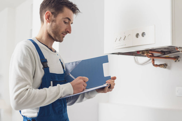 Professional plumber checking a boiler at home and writing on a clipboard - Photo, Image