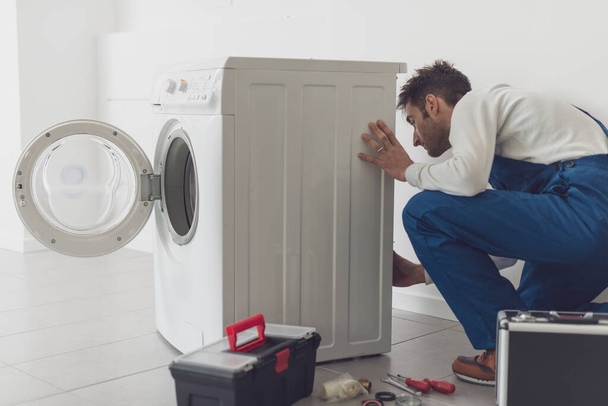 Repairman fixing a washing machine, he is adjusting a knob, professional service concept - 写真・画像