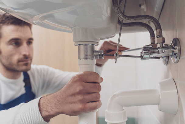 Professzionális vízvezeték szerelő javítás mosogató otthon, ő ellenőrzi csövek egy csavarkulcs - Fotó, kép