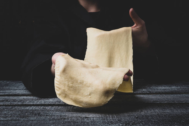 the chef is holding the dough on a dark background. thin dough for pasta. food preparation process - Photo, Image