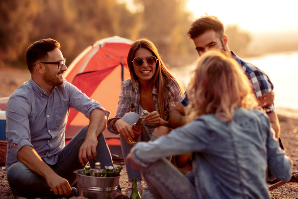 Grupa przyjaciół mających piknik w letni dzień, bawią się z piwami i gitarą. - Zdjęcie, obraz