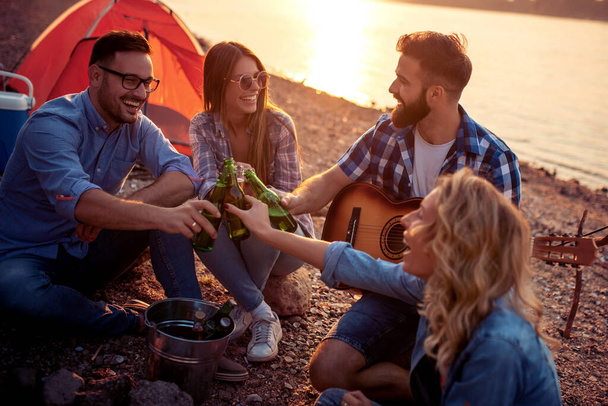Jonge vrienden die plezier hebben en bier drinken op het strand. - Foto, afbeelding