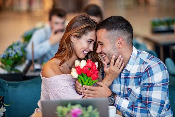 Atractiva pareja en la cafetería. Hombre dando tulipanes a su novia.Gente, amor y concepto de estilo de vida. - Foto, imagen