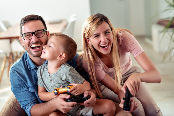 Ευτυχισμένη οικογένεια που παίζει βιντεοπαιχνίδια στο σπίτι και διασκεδάζει μαζί. - Φωτογραφία, εικόνα