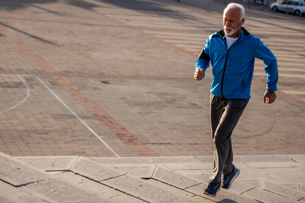 Homme âgé jogging dans la ville par une journée ensoleillée. Fitness, sport, personnes et mode de vie concept. - Photo, image