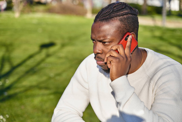 Retrato del joven afroamericano hablando por celular en un parque. Hombre negro con trenzas en el pelo.  - Foto, Imagen