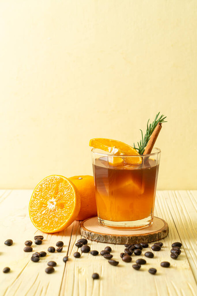 A glass of iced americano black coffee and layer of orange and lemon juice decorated with rosemary and cinnamon - Фото, изображение