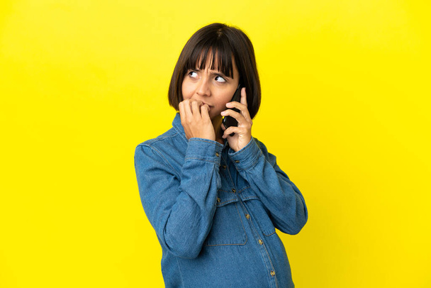 Pregnant woman using mobile phone isolated on yellow background having doubts - Photo, Image