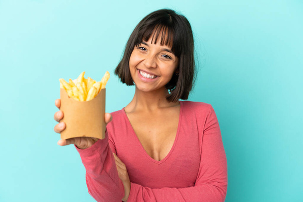 jong brunette vrouw holding gebakken chips over geïsoleerde blauw achtergrond - Foto, afbeelding