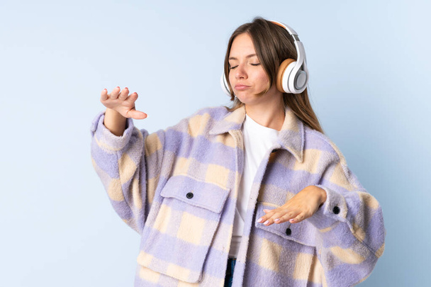 Young Lithuanian woman isolated on blue background listening music and dancing - Foto, Imagem