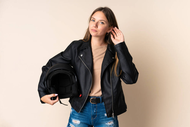 Young Lithuanian woman holding a motorcycle helmet isolated on beige background having doubts - Photo, Image