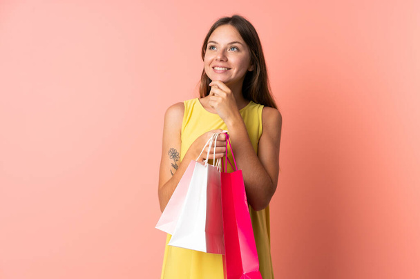 Молодая литовская женщина изолирована на розовом фоне, держит сумки с покупками и думает: - Фото, изображение