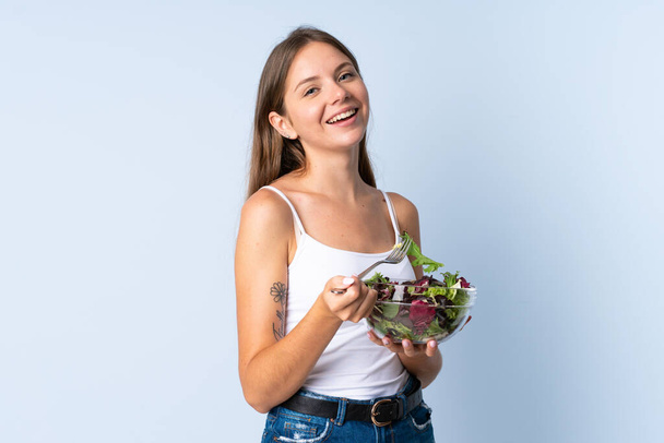 Young Lithuanian woman isolated on blue background holding a bowl of salad with happy expression - Zdjęcie, obraz