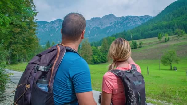Achteraanzicht van een man en vrouw op zoek naar een bergachtig landschap en wijzend naar iets aan de horizon tijdens een trekking. - Video