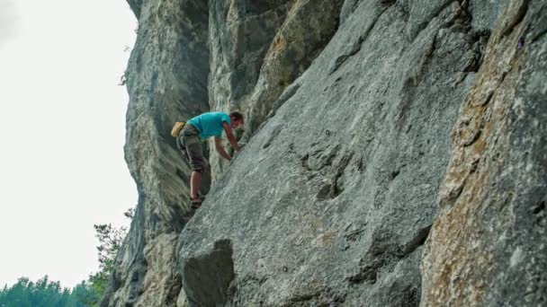 Hombre caucásico subiendo la montaña, trabajando en la cuerda, atado al arnés y apoyado hacia atrás - Metraje, vídeo