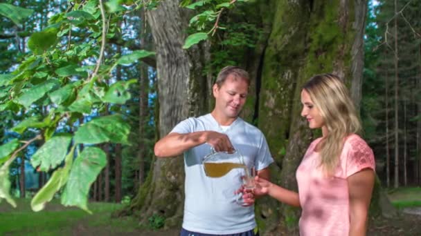 Een man schenkt een drankje in op een vrouw en zichzelf in een bos.. - Video