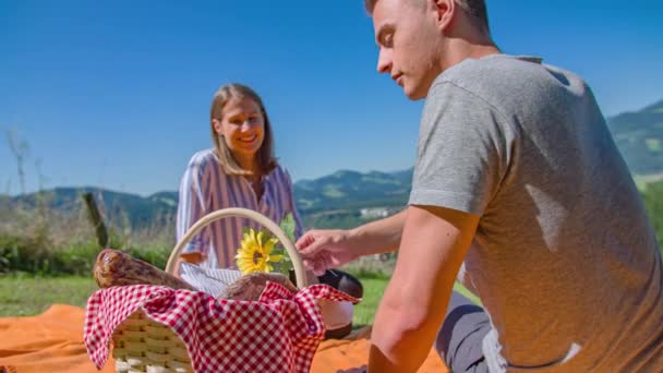 mladý muž nabízí květinu a flirtovat během pikniku na trávě - Záběry, video