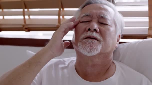 Ázsiai idős férfi fejfájással ül az ágyon reggel - Felvétel, videó