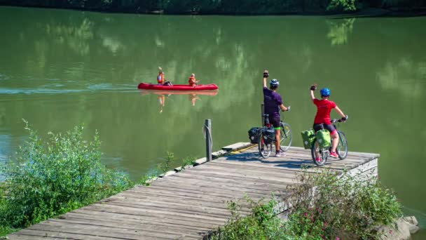 два велосипедиста, що махають від дерев'яного пірсу до пари друзів на байдарках на річці
 - Кадри, відео