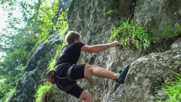 Nuori seikkailunhaluinen kalliokiipeilijä, joka kiipeää jyrkkiä kiviä ilman köysiä. Seikkailun ja extreme-urheilun käsite. Näkymä alhaalta. - Materiaali, video