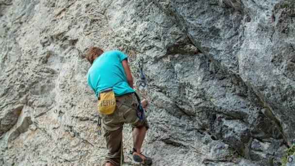 Nuori seikkailunhaluinen vuorikiipeilijä, joka kiipeää jyrkkää ja kivistä vuorta pitkin. Seikkailun ja extreme-urheilun käsite. Näkymä alhaalta. - Materiaali, video