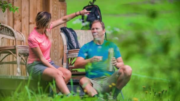 Wanderer-Paar in der Nähe eines Holzhauses im Wald entspannt sich und trinkt. - Filmmaterial, Video
