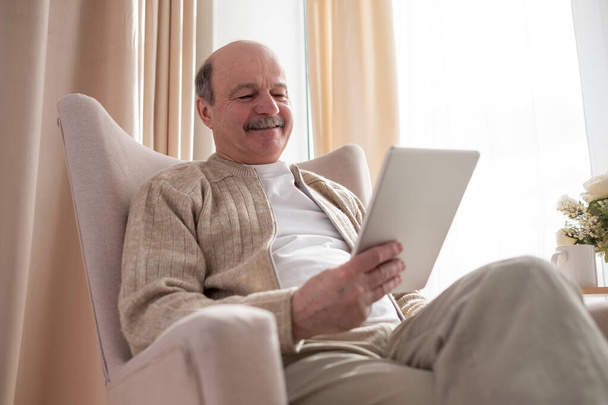 Старший чоловік в дивані з планшетним комп'ютером вдома
 - Фото, зображення