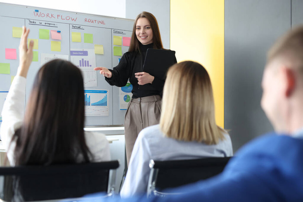 Женщина бизнес-тренер стоит возле доски и задает вопрос слушателю - Фото, изображение
