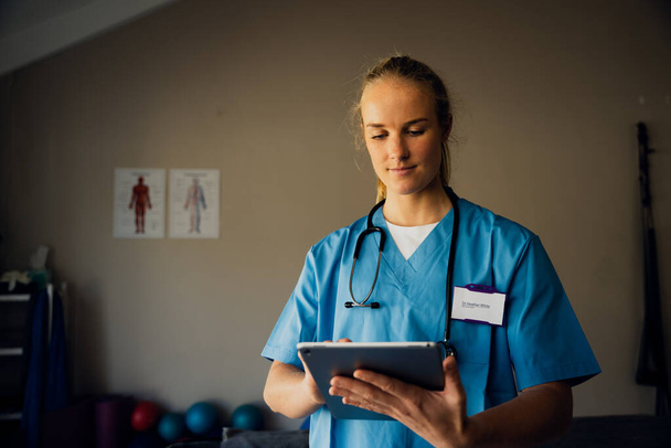 Caucasian nurse preparing for online consultation with sick patient using digital tablet standing in clinic  - Foto, imagen