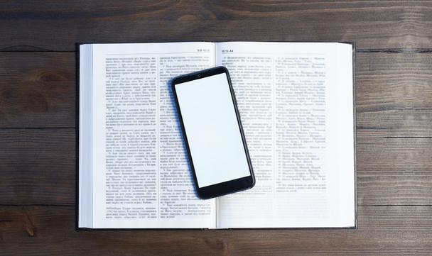 Das aufgeschlagene Bibelbuch auf einem Holztisch. Gebet. Telefon auf dem Buch. Leerer Bildschirm. Arbeitsplatz im Büro. - Foto, Bild