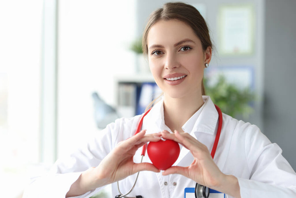 Smiling woman doctor holding red toy heart in her hands in clinic - Foto, immagini