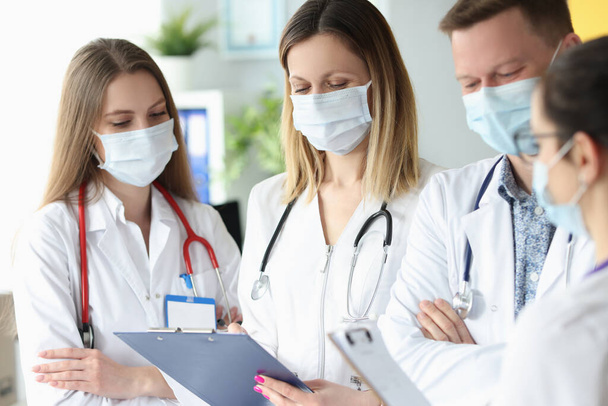 Koruyucu tıbbi maskeli bir grup doktor ellerinde belgelerle klinikte duruyorlar. - Fotoğraf, Görsel