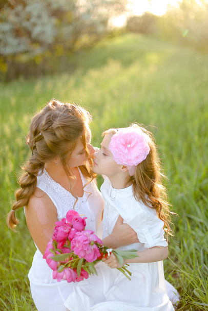 Portrait of young happy mother kissing little daughter in grass. - 写真・画像