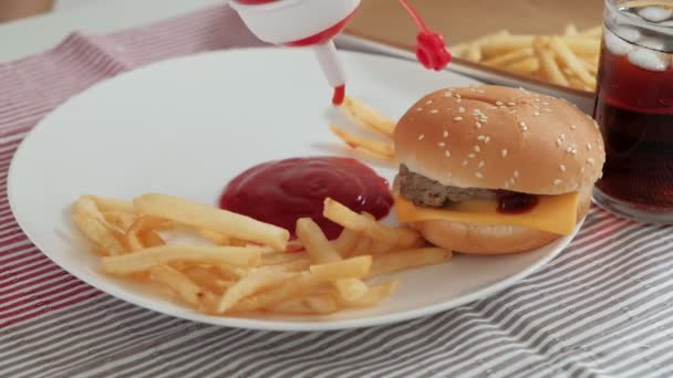 Imágenes de cerca: Ketchup en un plato blanco en manteles que se vierten de botellas rojas para bocadillos de comida chatarra poco saludables, incluyendo hamburguesas para llevar, papas fritas, bocadillos y cola. - Metraje, vídeo