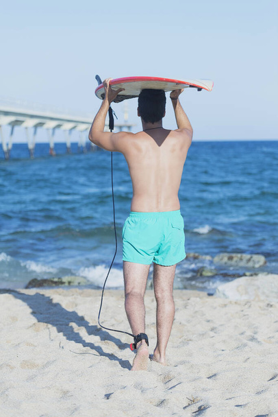 Sexy Wassersport Fitness Bauchtrainer trägt sein Surfbrett auf dem Kopf. - Foto, Bild