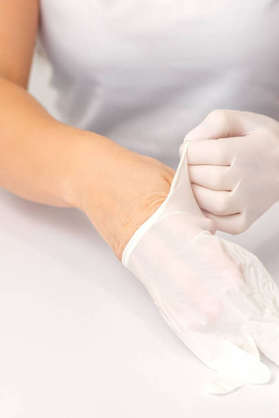 Il primo piano delle mani dell'infermiere o del medico donna indossa guanti protettivi di gomma bianca sul tavolo. - Foto, immagini