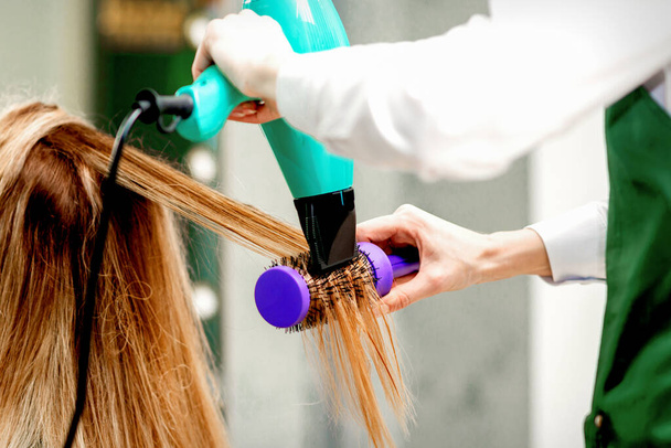 Rückansicht einer jungen Frau, die in einem Friseursalon mit Haartrockner und Haarbürste Haare trocknet - Foto, Bild
